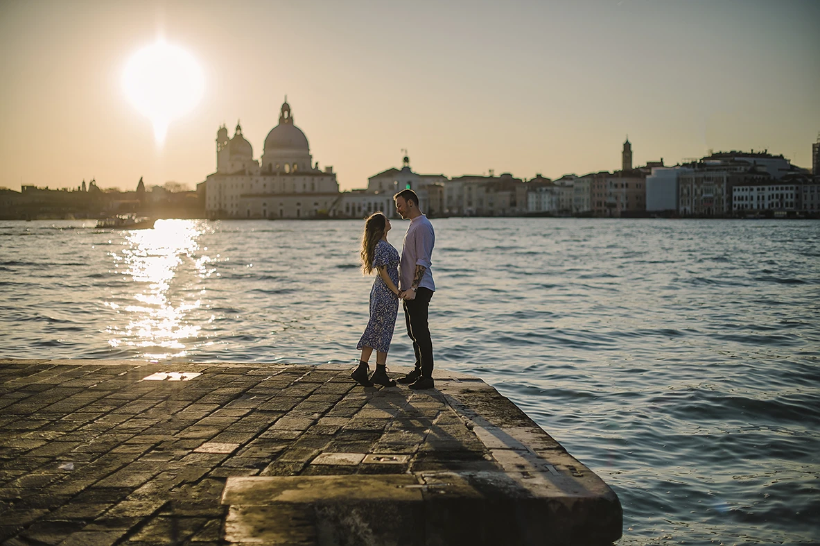 An intimate kiss of Barth and Maria as they stand by the Grand Canal, their silhouettes framed against the twinkling lights of evening Venice