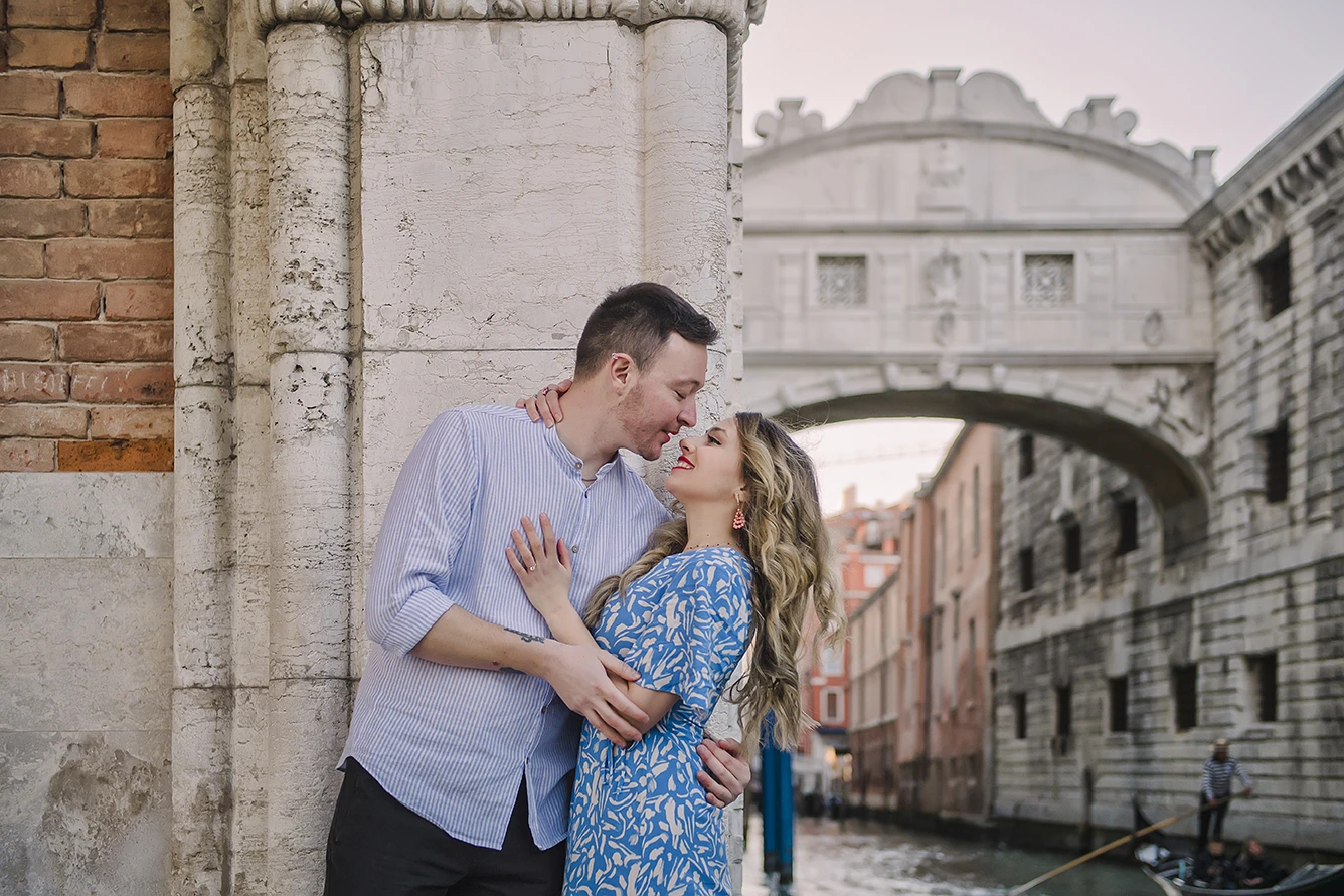 he fiancés share a gentle kiss  with the historic buildings of Venice and boats passing by in the soft, fading light of dusk