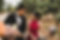 A couple smiles at each other in a park. The man in a black suit holds stuffed toys, while the woman in a red dress holds a bike with flowers for wedding photography