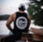 A man wearing an Illbury and Good tank top sits with his back to the camera at a lake.