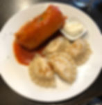 A plate of food with a cabbage roll covered in orange sauce, four pierogies, and a small dish of sour cream.