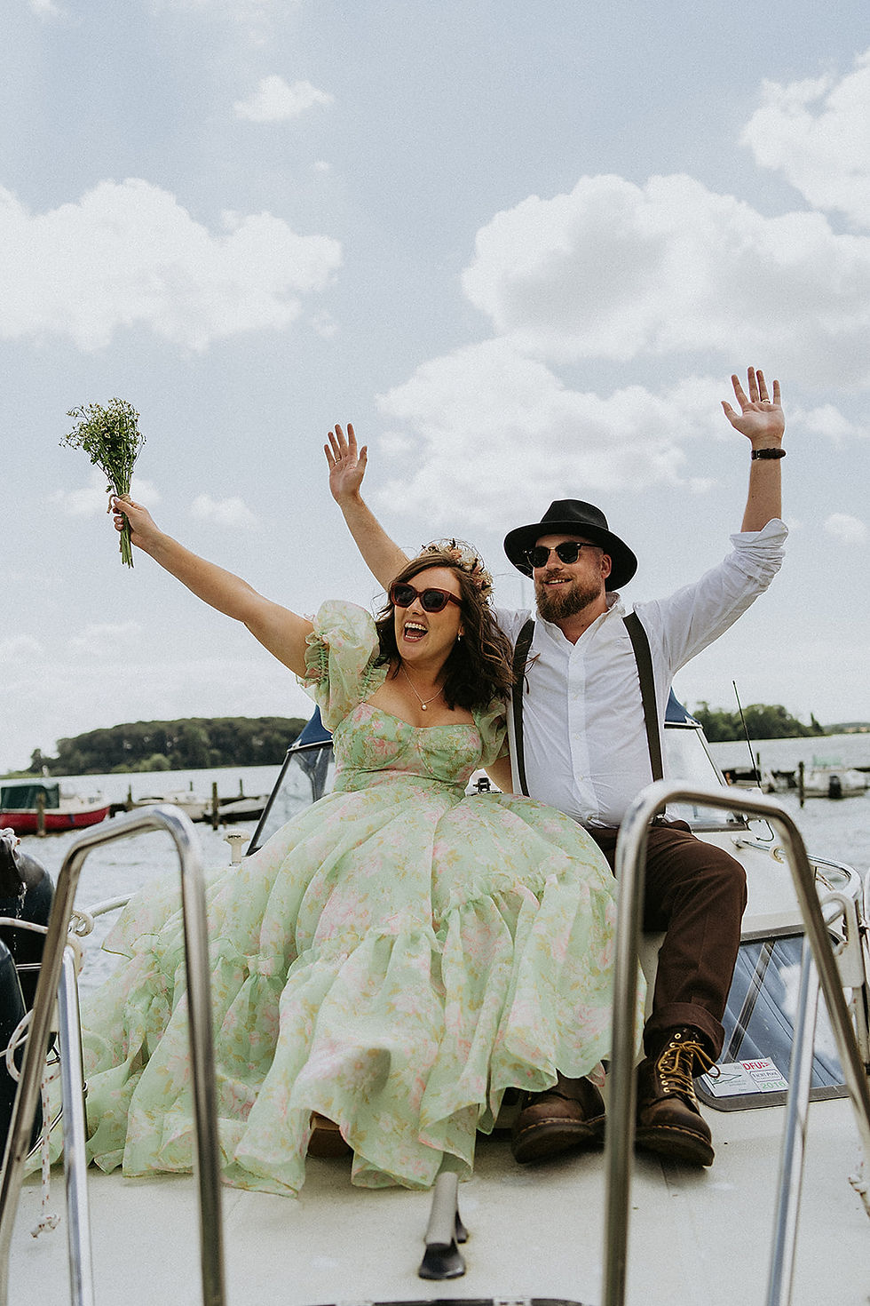 Joyful newlyweds celebrating on a boat after their wedding in Denmark, with the bride wearing a colourful floral non-white wedding dress for an adventurous Scandinavian elopement.