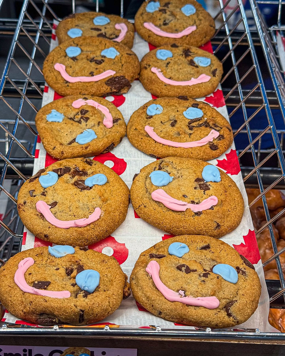 Chocolate chip cookies with blue and pink icing smiles on a metal rack, set on red and white paper, creating a cheerful mood.