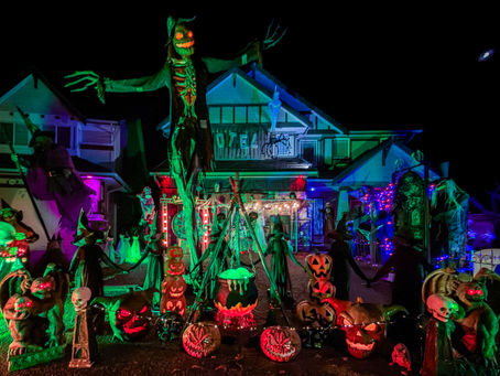 Halloween display at 1066 Amazon Drive, Port Coquitlam, with a towering scarecrow, witches, glowing pumpkins and a cauldron lit at night.