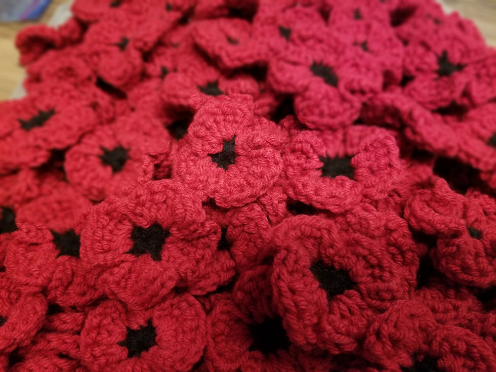 Close-up of red knitted poppy flowers with black centers, layered together. The setting is a warm, textured background.
