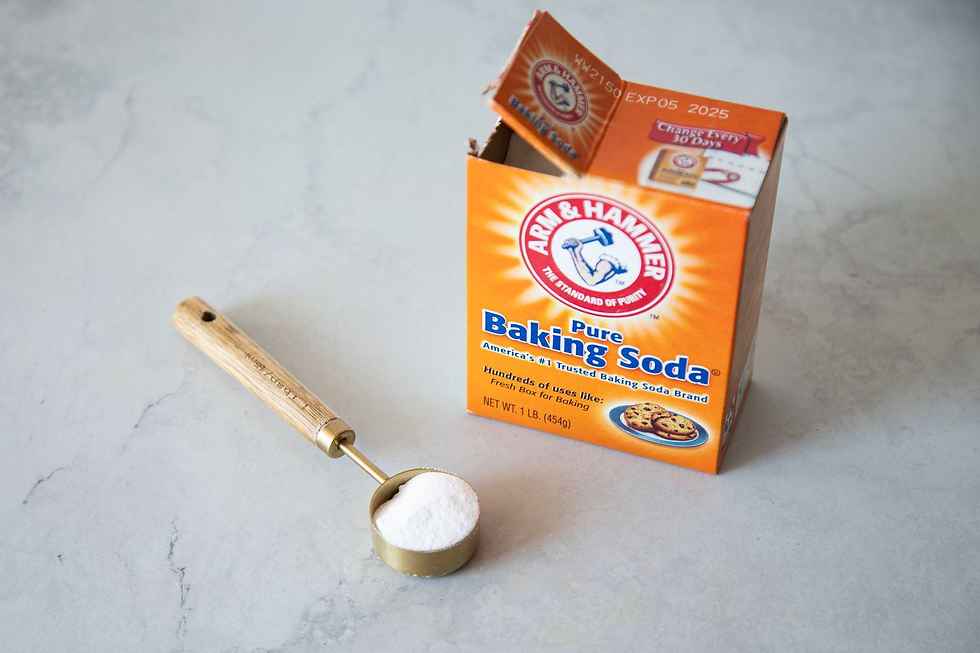 Box of Arm & Hammer baking soda with a gold measuring spoon filled with soda on a marble surface. Bright orange packaging, open top.