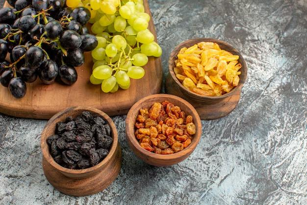 Bowls of black, golden, and brown raisins in wooden bowls. Fresh black and green grapes on a wooden tray. Rustic gray textured background.