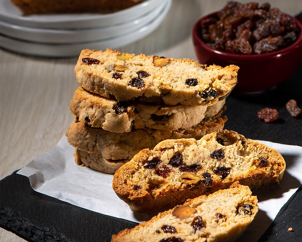 Stack of biscotti with raisins and nuts on parchment paper, set on a slate board. A bowl of raisins is in the background. Warm, inviting tone.