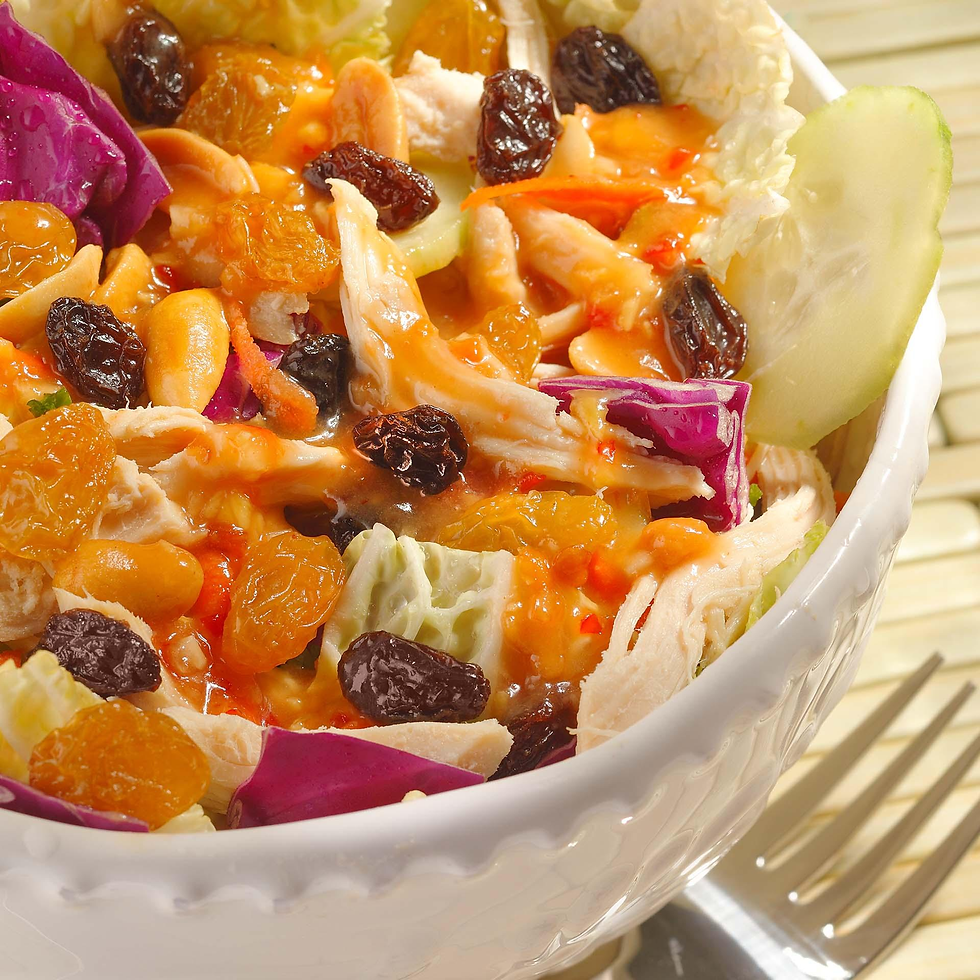 Colorful salad in a white bowl with raisins, peanuts, shredded chicken, and purple cabbage. Fork on the bamboo mat background.