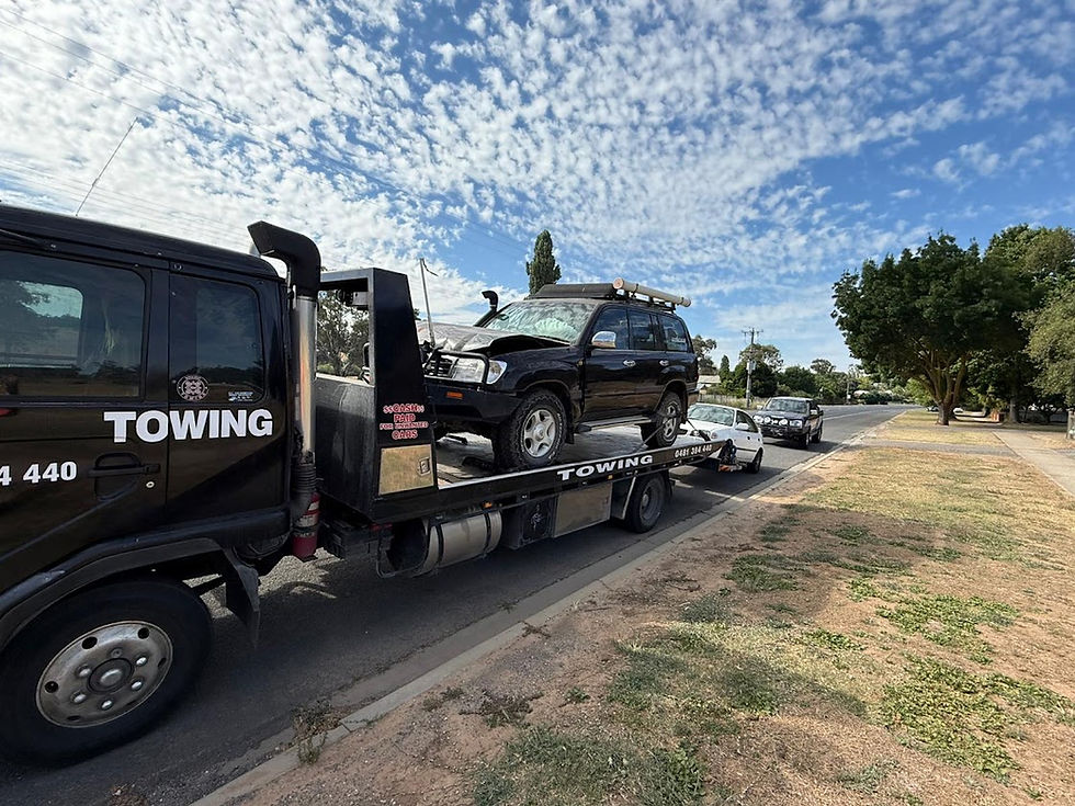Black tow truck carrying a damaged SUV on a flatbed.