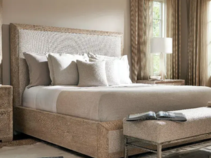Beige cozy bedroom with a large bed, pillows, a bench with a book, nightstands, lamps, and windows with curtains, creating a cozy, tranquil vibe.