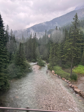 Banff National Park colorful stream and mountains on a rainy day as seen from the Rocky Mountaineer train.