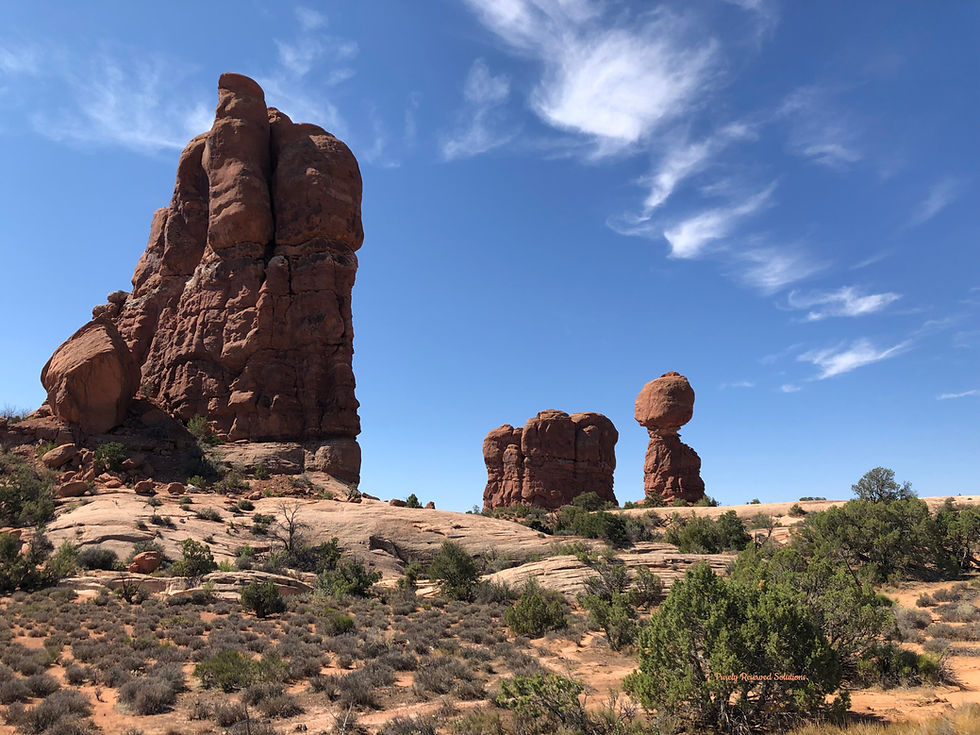 Balancing Rock in Arches National Park. Red rock formations under a clear blue sky in a desert landscape, with sparse vegetation and scattered clouds, create a tranquil scene.