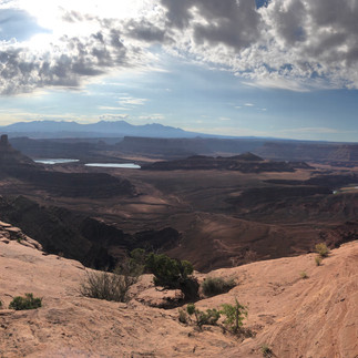 Dead Horse Point State Park. Cloudy blue skies with the morning sun peeking through over red rock canyons and water in the distance.