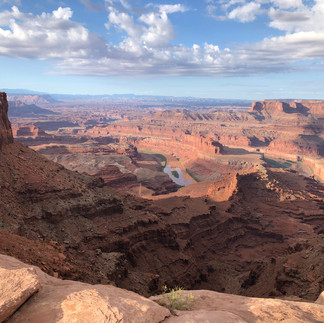 Dead Horse Point State Park. Colorful red rocks canyon under cloudy blue skies with red, pink and brown rock formations and river snaking though.