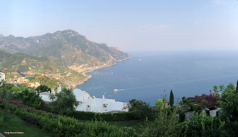 Coastal landscape with lush greenery, white buildings, and distant mountains. Calm View of the Tyrrhenian Sea from our Airbnb on the Amalfi Coastal town of Ravello with boats moored. Bright, serene atmosphere.