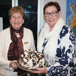 Volunteer Renata presenting her famous chocolate cake to prize winner