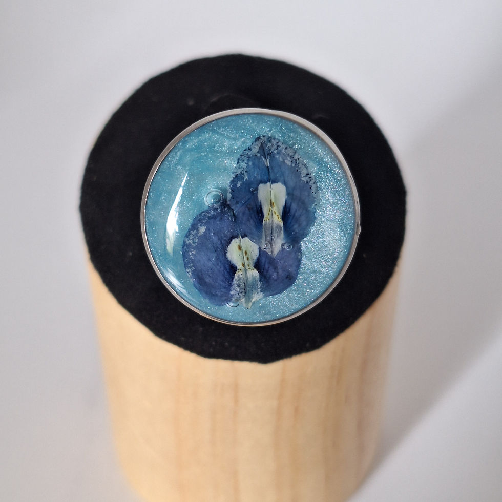 Close-up of a preserved Texas bluebonnet adjustable ring with stainless steel hardware and shimmering blue background