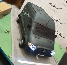 Hyper‑realistic Amazon Prime van cake with lit headlights displayed on a road‑themed cake board.