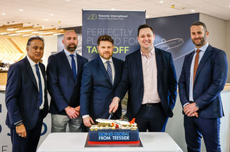Corporate celebration cake with the message “Going Global from Teesside,” displayed at a Teesside International Airport business event with executives standing behind it.