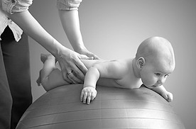 Kinderphysio frau massiert ihr baby auf einem lila ball blauer hintergrund in Graustufen