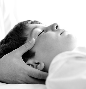 Kinderphysiotherapie weibliche Physiotherapeutin massiert Kind den Kopf in Graustufen