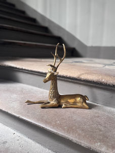 Vintage brass deer figurine with antlers in a reclining pose.