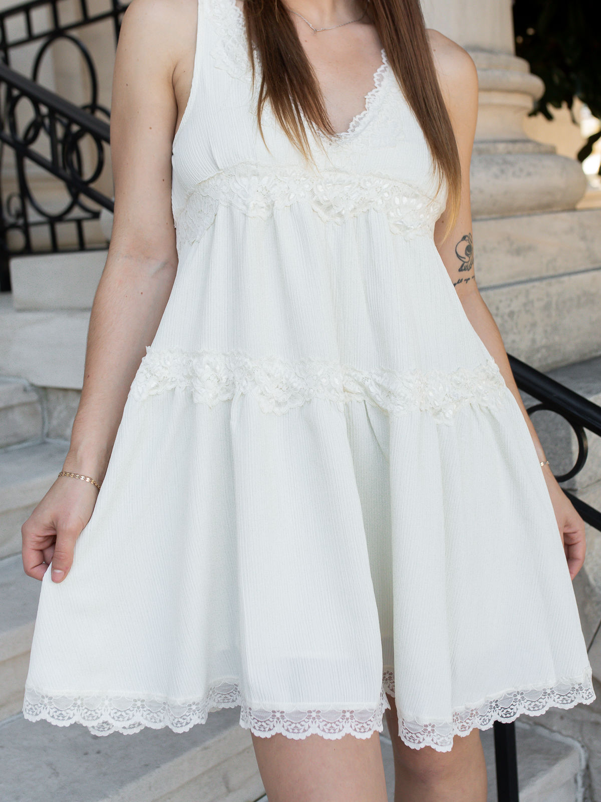 Model wearing the Vivi Mini Woven Dress in Cream featuring a sleeveless V-neckline, floral lace detailing, and a flowy tiered