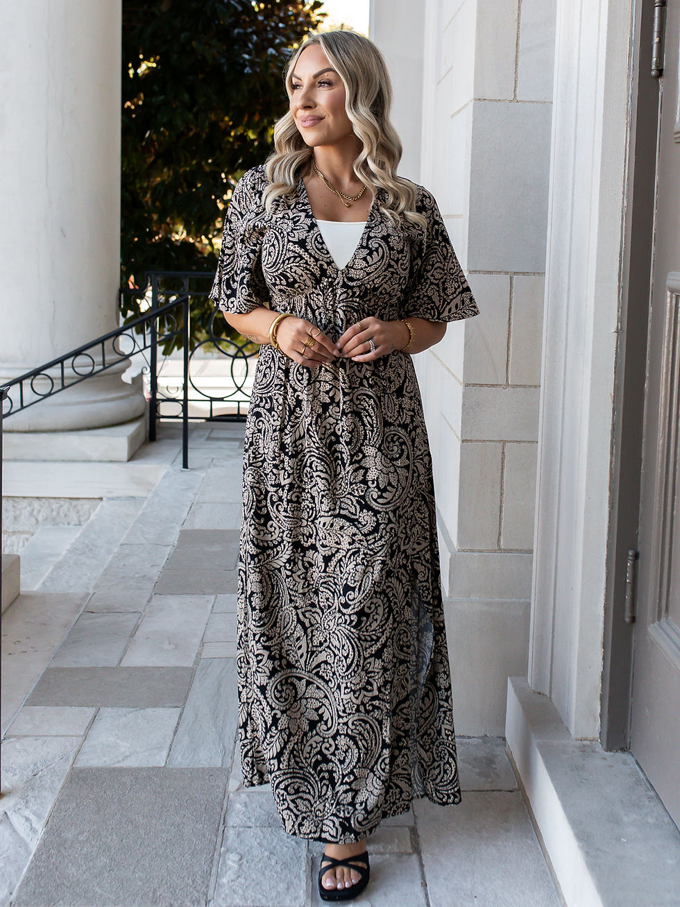 Model wearing the Violetta black paisley print midi dress with black heeled sandals.