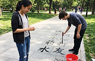High school students practice authentic Chinese water calligraphy using plain water and a traditional calligraphy brush outdoors.