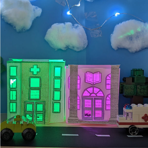 Thumbnail: Photo of the 3 fully assembled STEAM kits, featuring decorated paper buildings with functioning circuits