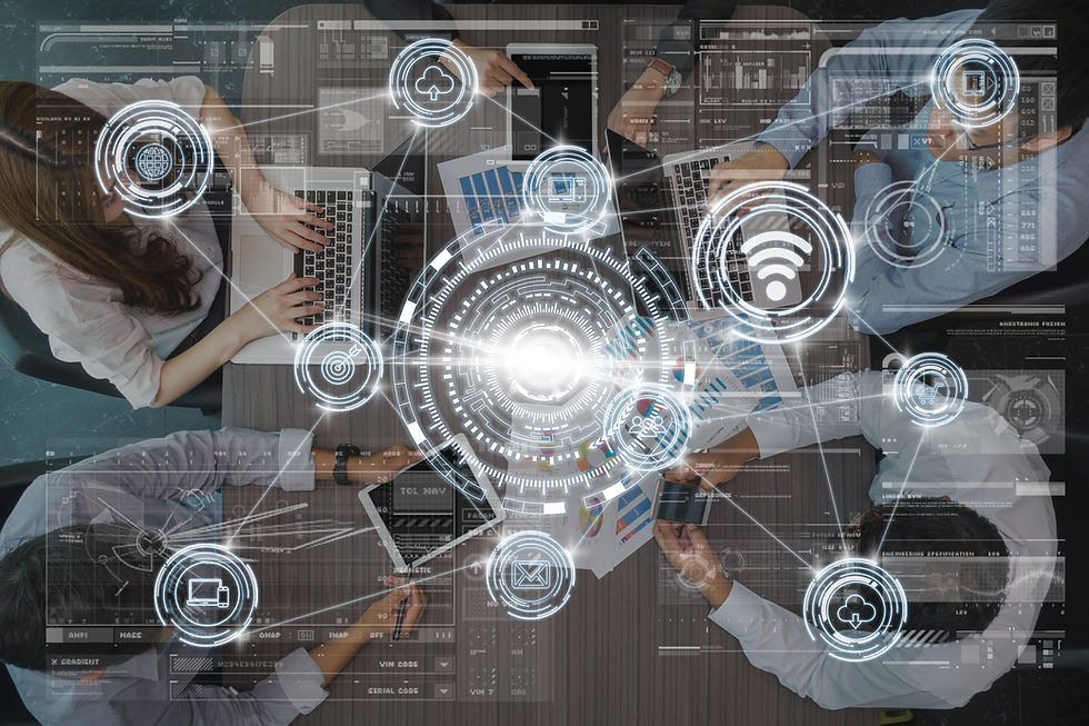 Top view of four people around a table working on laptops and tablets. Digital icons overlay the image, creating a futuristic tech ambiance.