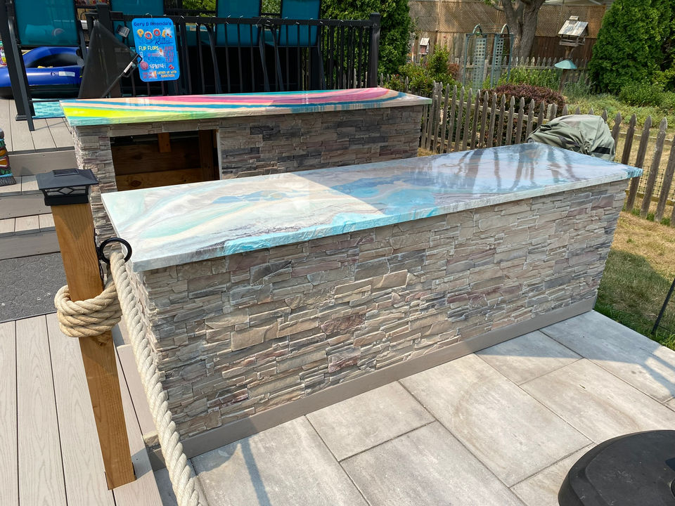 Custom epoxy countertops steal the show, with one mimicking stunning blue quartzite and another rocking a bold, tie-dye vibe. Paired with a sleek brick facade, this outdoor kitchen is as functional as it is eye-catching.