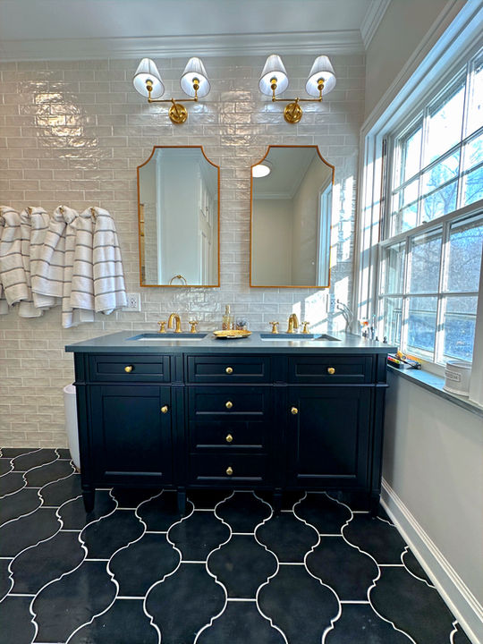 Luxury bathroom vanity with black marble countertop, double white undermount sinks, brass cross-handle faucets, glossy gray subway tile backsplash, and gold leaf tray accents
