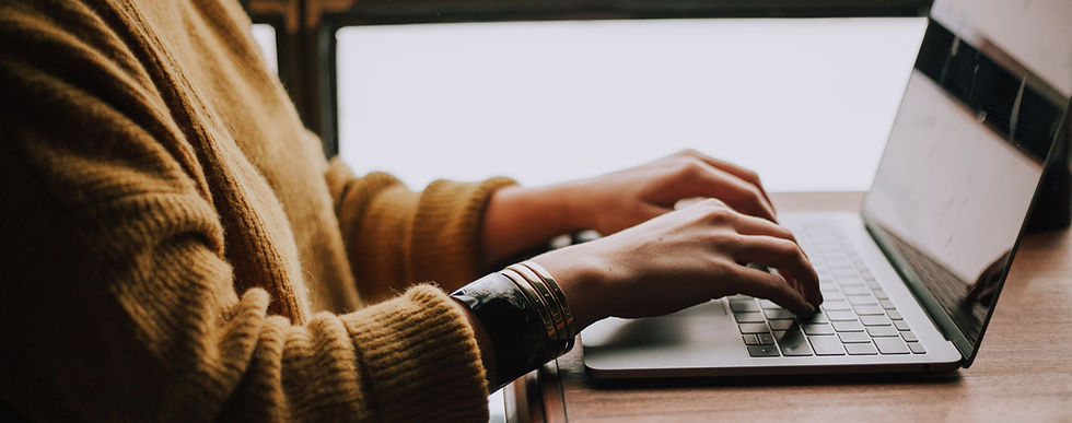 A person in a woolen jumper and simple metal bracelets types on a laptop on a wooden table.
