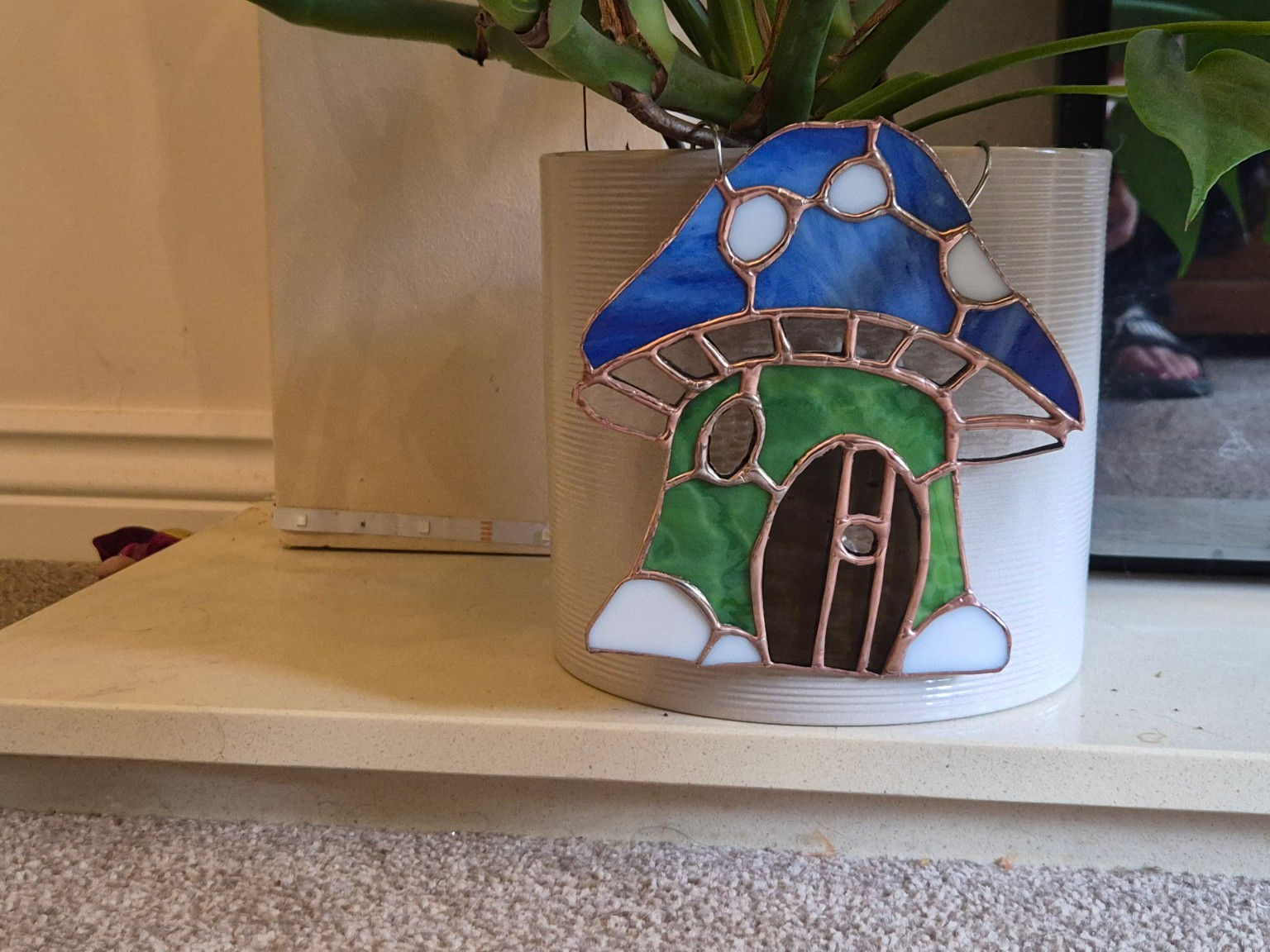 Handmade stained glass mushroom fairy door plant pot hanger displayed on an indoor houseplant pot