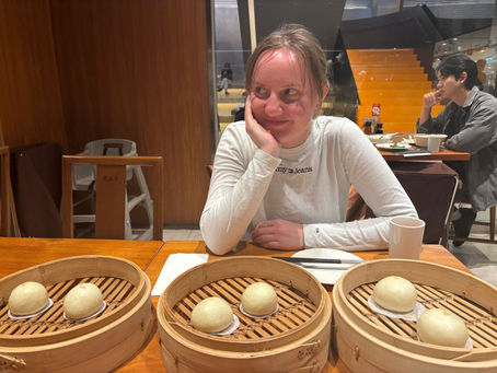Author seated at a Din Tai Fung restaurant in Taiwan, with bamboo steamers of xiaolongbao placed on the table.