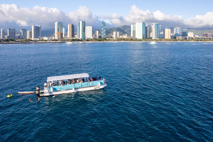 Aerial view of a boat cruising the Hawaiian seas with the cityscape of  Honolulu in the background