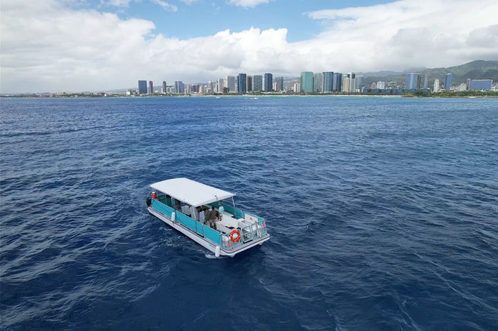 Above view of a boat navigating through Hawaiian seas with the stunning backdrop of Waikiki and Honolulu.