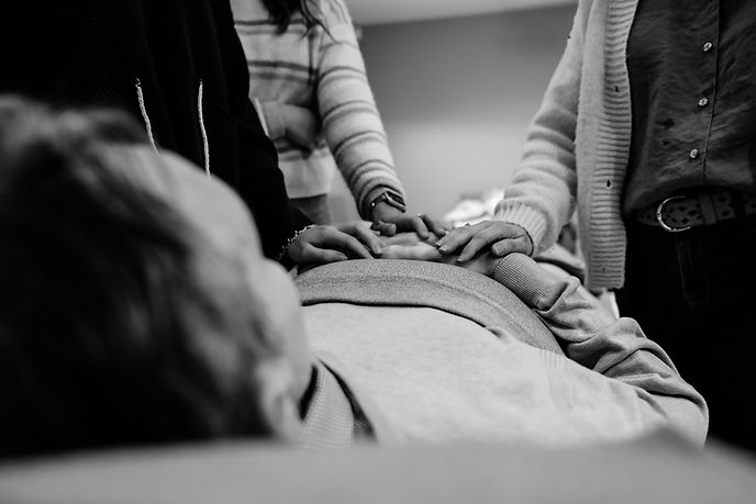 Handen die rusten op een lichaam tijdens een afscheid, als teken van nabijheid en verbondenheid.