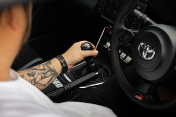 David Foo, Founder of Road Pilgrim, sits in the driver's seat of the Toyota GR86 with his hand on the manual shifter
