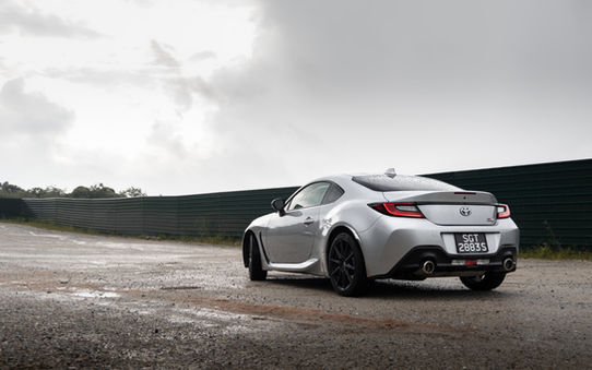 Diagonal rear end view of the Toyota GR86 in Singapore parked along a dirt track with parting clouds in the distance