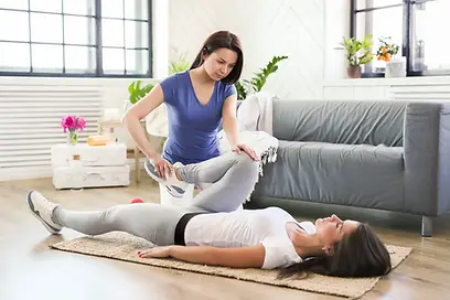 A physical therapist in a blue shirt performing a guided hip mobility and stretching exercise on a patient lying on a yoga mat.