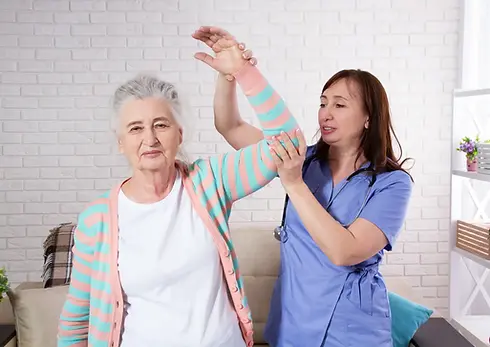 Physiotherapist helping an elderly woman with shoulder mobility exercises in a home setting.