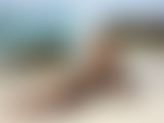 Alexandra Levchuk sitting on a beach with waves behind her, illustrating a blog about remote work productivity and how creative work thrives outside the office.