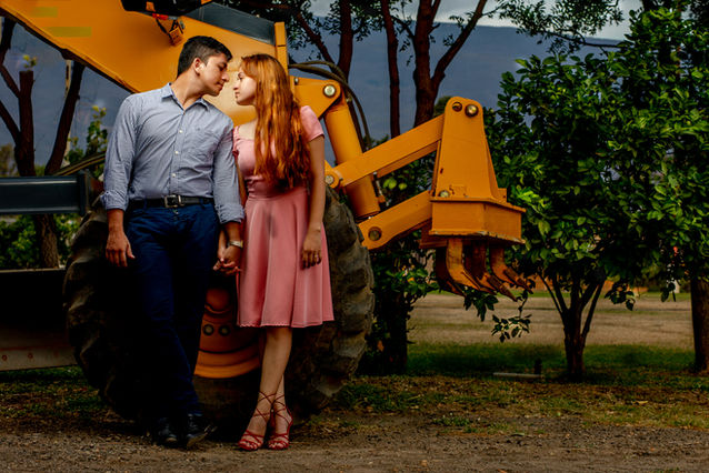 Pareja a punto de besarse, sonriendo, junto a una máquina amarilla. Fotografía de bodas