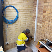 Electrician in high-vis running cabling along a brick wall during an office electrical upgrade at Modnt Tech, Balcatta.