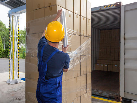 A worker hand wraps a pallet with stretch wrap