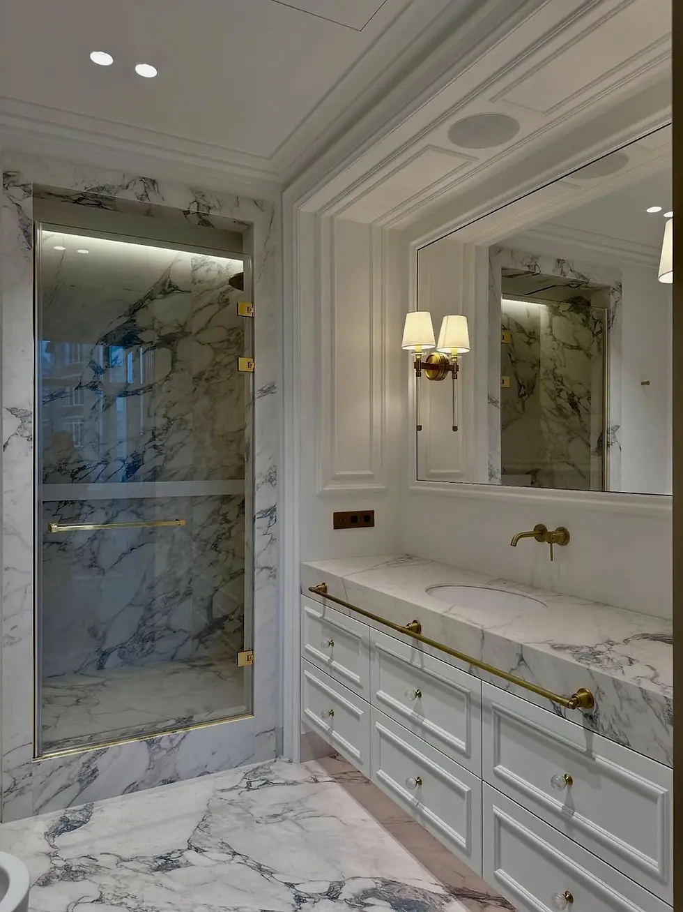 Elegant marble bathroom with white cabinets, gold fixtures, large mirror, and glass shower. Soft lights create a luxurious ambiance.