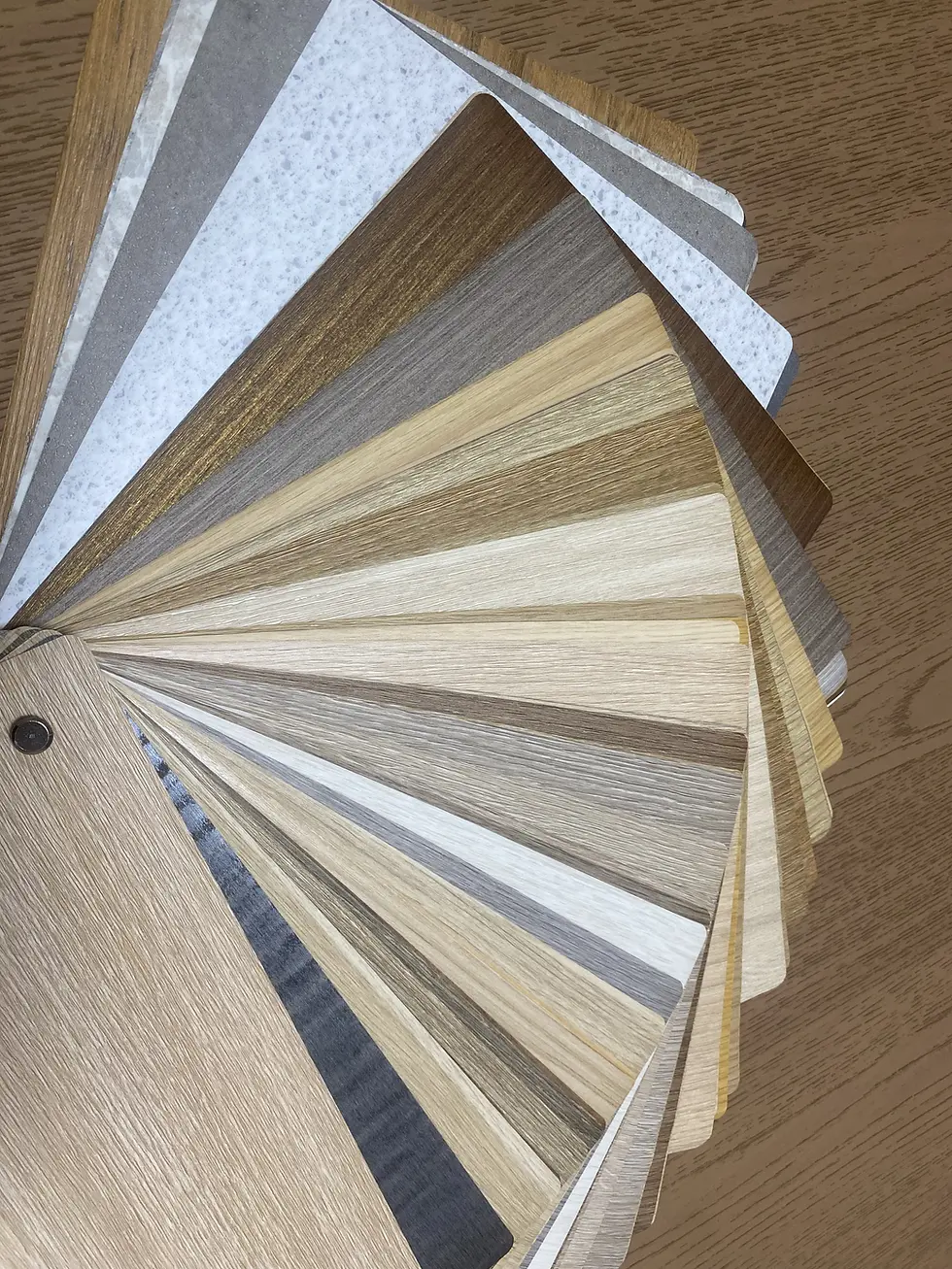 A fan of wood and stone laminate samples in various shades on a wooden surface, showcasing a range of textures and neutral colors.